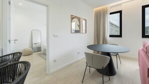 Ein modernes Hotelzimmer mit rundem Tisch, zwei Stühlen, einem Bett und einem großen Fenster mit Blick auf Gebäude.