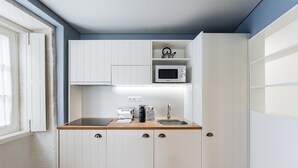 Una cocina compacta con muebles blancos, microondas, tetera y tostadora.