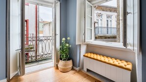 Una habitación con piso de madera, un banco blanco, una planta en maceta y un balcón con ventana.
