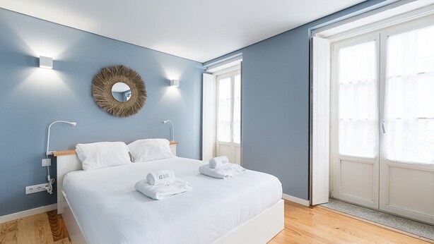 Un dormitorio con cama, dos mesitas de noche, un espejo en la pared y ventana con vistas.