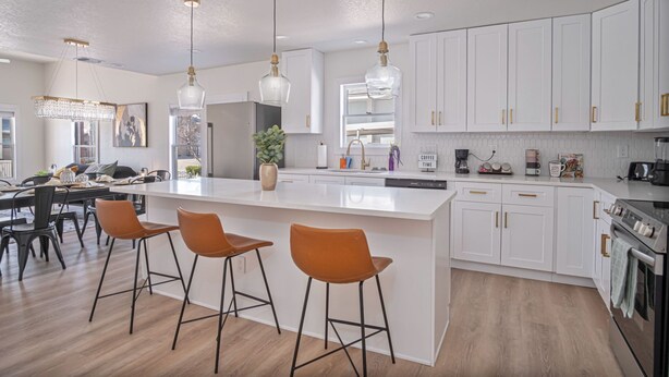 A modern kitchen with white cabinets, a large island with stools, pendant lights, and a built-in oven. - Create Memories 4BR 3BA Near Riverwalk Downtown (San Antonio)