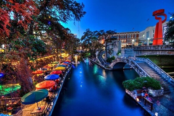 A riverside restaurant with outdoor seating and a bridge.