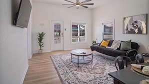 A living room with a ceiling fan, a black sofa with cushions, a coffee table, and a dining table with chairs. - Create Memories 4BR 3BA Near Riverwalk Downtown (San Antonio)
