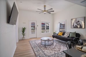A living room with a ceiling fan, a black sofa with cushions, a coffee table, and a dining table with chairs.
