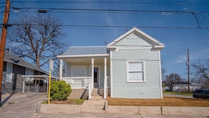 A light blue single-story house with a front porch, a covered entryway, and a small front yard. - Create Memories 4BR 3BA Near Riverwalk Downtown (San Antonio)
