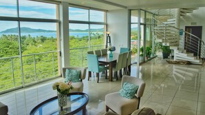 A spacious living area with a large window offering a view of a lush landscape and a body of water. - Duplex Penthouse with Ocean View in Tamarindo, 5 min walk to the beach (Tamarindo)