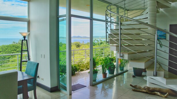 A spacious room with a modern staircase, large windows offering a view of the sea, and a dog lying on the floor. - Duplex Penthouse with Ocean View in Tamarindo, 5 min walk to the beach (Tamarindo)
