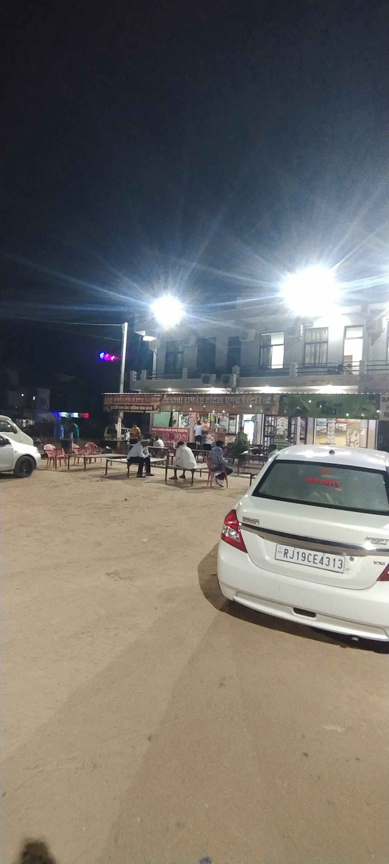 A parking lot with a white car and several people sitting on benches.