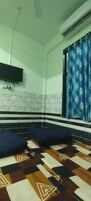 Una habitación con piso estampado, un televisor de pantalla plana en la pared, una ventana con cortinas azules y un ventilador de techo.