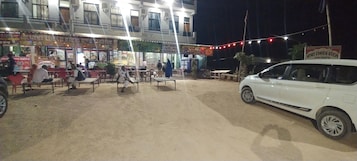 Hotel con terraza al aire libre y un coche blanco estacionado adelante.
