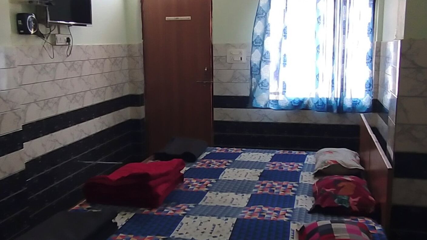 Une pièce avec un lit, une couette, une couverture rouge, un téléviseur et une fenêtre avec des rideaux.