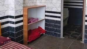 Ein Zimmer mit einem Bett, einem Holzregal mit gefalteter Kleidung und einer Tür zu einem Badezimmer.