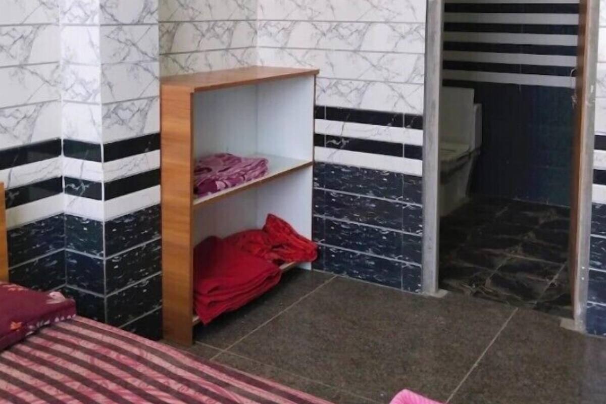 Una habitación con una cama, un estante de madera con ropa doblada y una puerta que da a un baño.