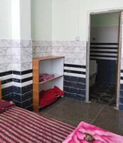 Una habitación con una cama, un estante de madera con ropa doblada y una puerta que da a un baño.