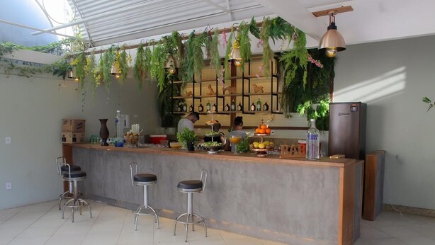 Uma cozinha moderna com espaço para bar, plantas penduradas, uma geladeira e banquetas.
