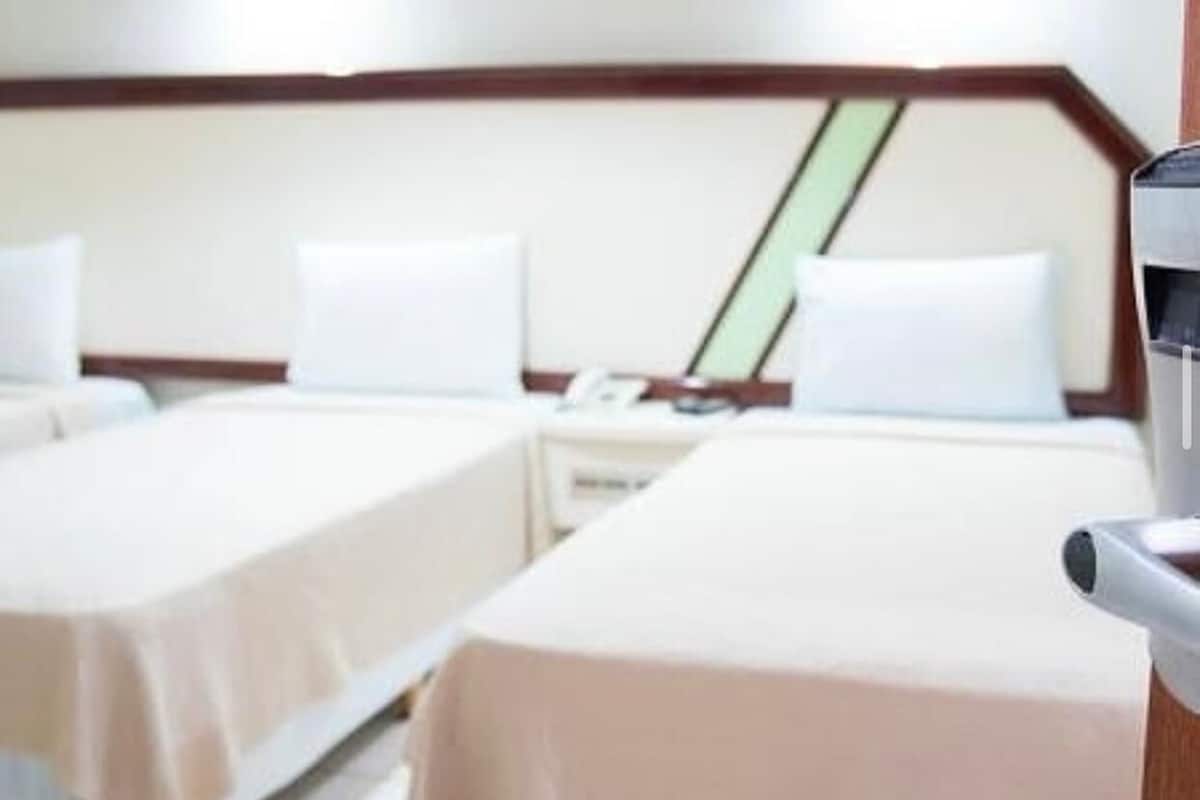 A hotel room with two single beds, a bedside table with a lamp, and a small desk with a chair.