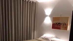 Quarto com cama, um banquinho, mesa de cabeceira e uma obra de arte na parede.