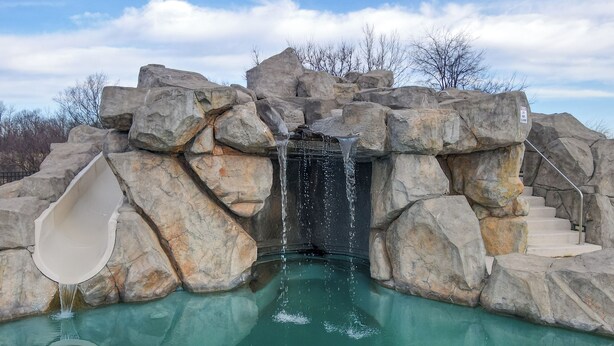 A rock formation with a water slide and a pool.