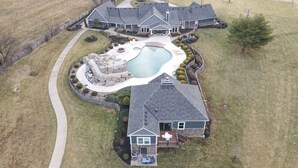 A large, two-story house with a swimming pool, a deck, and a stone patio.