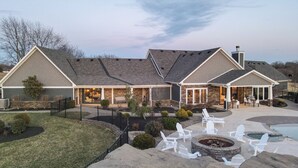 A two-story house with a stone facade, a covered patio with Adirondack chairs, and a fire pit.