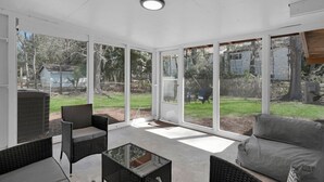 A sunlit patio with wicker furniture, large sliding glass doors, and a view of a backyard.