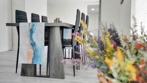 A modern dining area with a wooden table and chairs, a vase of flowers, and a painting on the table.