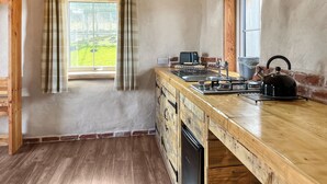 Une cuisine avec des meubles de rangement en bois, un évier en acier inoxydable, une bouilloire et une fenêtre avec des rideaux.