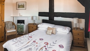 A bedroom with a large bed, two bedside tables, a chair, a fireplace, and a picture on the wall. - 2 bedroom accommodation in Weobley, Herefordshire (Weobley, Herefordshire)