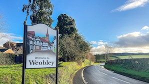 A welcome sign for Weobley with a depiction of a traditional building and a church tower. - 2 bedroom accommodation in Weobley, Herefordshire (Weobley, Herefordshire)