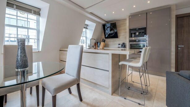 Een moderne keuken met een glazen eettafel, barstoelen en een ingebouwde televisie.