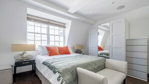 Een slaapkamer met een groot bed, nachtkastjes, een stoel, een raam en een kledingkast.