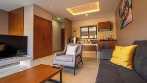Ein modernes Wohnzimmer mit Flachbildfernseher, grauem Sofa mit gelbem Kissen, grauem Sessel und Couchtisch aus Holz.