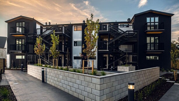 Un immeuble résidentiel moderne à plusieurs étages, doté de balcons, d’un jardin aménagé et d’un chemin piétonnier pavé.