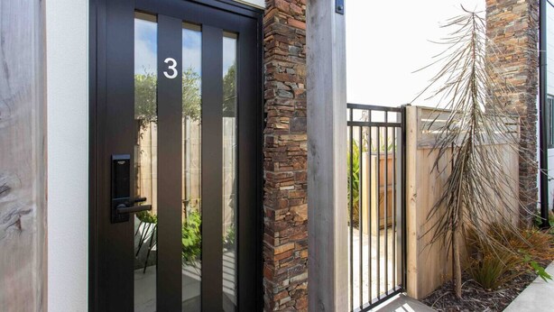 A modern house with a black door marked with the number 3, a stone pillar, and a metal gate.