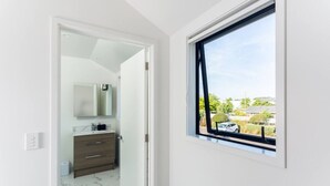 A bathroom with a white vanity, a mirror, and a window with a view of a residential area.