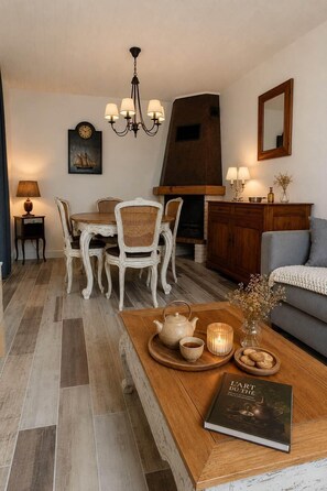 A dining area with a wooden table, white chairs, a chandelier, and a fireplace.