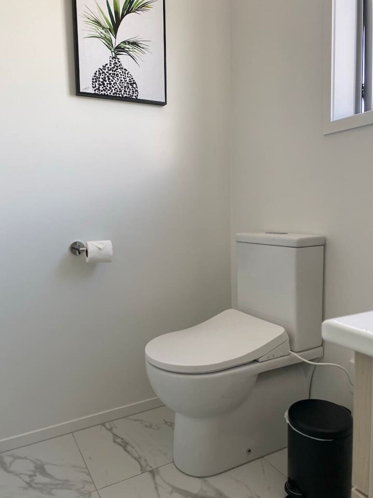 A modern bathroom with a toilet, a trash bin, and a framed picture on the wall.