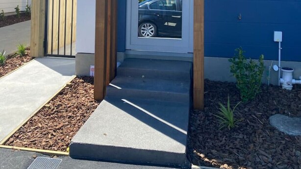 Un edificio moderno con fachada azul, entrada de madera y un coche estacionado en la entrada.