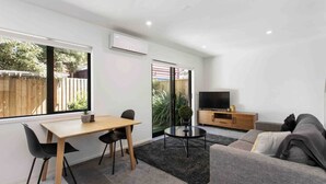 A modern living room with a dining area, a sofa, a TV, and a sliding glass door leading to a garden. - Relax Unwind Super Fast Internet (Christchurch)