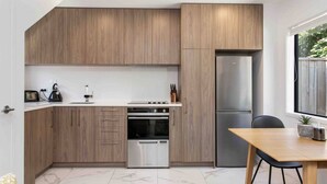 A modern kitchen with wooden cabinets, a stainless steel refrigerator, a built-in oven, and a dining area with a table and chairs. - Relax Unwind Super Fast Internet (Christchurch)