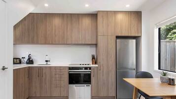 A modern kitchen with wooden cabinets, a stainless steel refrigerator, a built-in oven, and a dining area with a table and chairs.