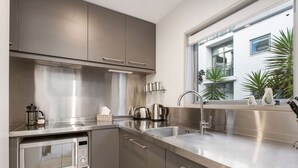 Une cuisine moderne dotée d’appareils électroménagers en acier inoxydable, d’un lave-vaisselle intégré et d’une fenêtre offrant une vue sur un bâtiment et des plantes à l’extérieur.