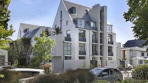 Un immeuble moderne à plusieurs étages, doté de balcons, entouré de verdure et bordé de voitures garées.