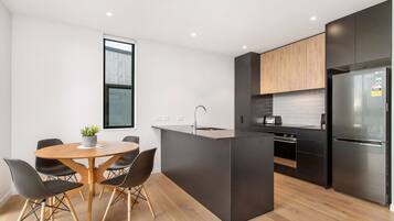 A modern kitchen with a central island, black cabinetry, and a stainless steel refrigerator.