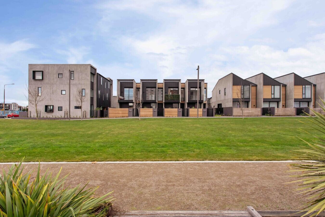 A modern building with a flat roof, multiple windows, and a grassy area in front.