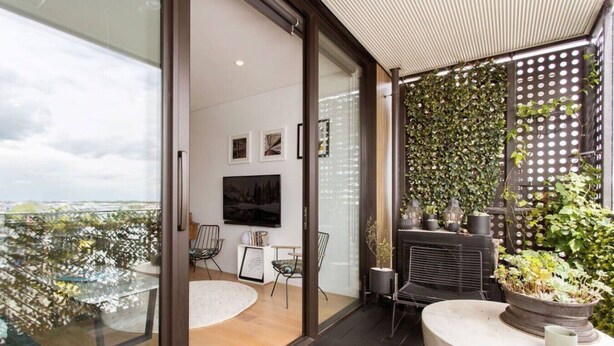 A modern balcony with a glass door, a flat-screen TV, a seating area with chairs, and a wall of greenery. - Whow! Unique Quirky Spacious Free Off Street Park (Christchurch)
