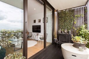Un balcón moderno con puerta de vidrio, televisor de pantalla plana, zona de estar con sillas y una pared cubierta de follaje.