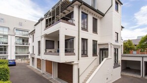 Un moderno edificio residencial de varios pisos con balcones, una zona de estacionamiento techada y una escalera que conduce a la entrada.