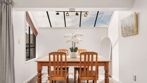 Un comedor con mesa y sillas de madera, una orquídea en maceta y un tragaluz.