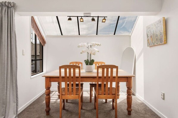 A dining area with a wooden table and chairs, a potted orchid, and a skylight above.